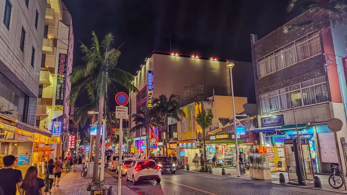 Illuminated shop signs and palm trees on Kokusai Street at night
