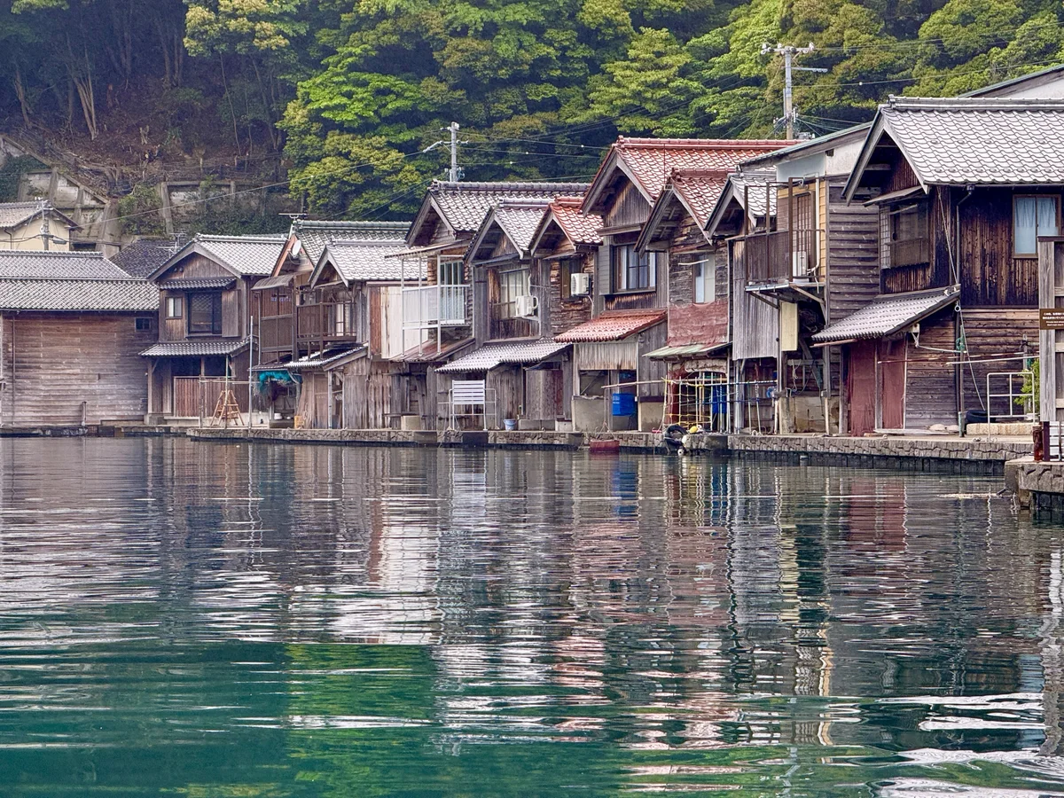 Ine's timber boathouses reflected in dark water in soft light on a rainy day