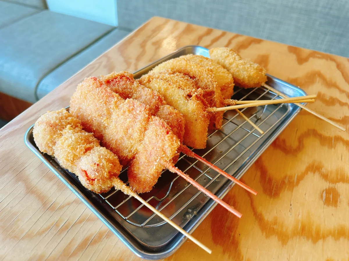 Illustrative photograph of breaded fried skewers on a metal tray