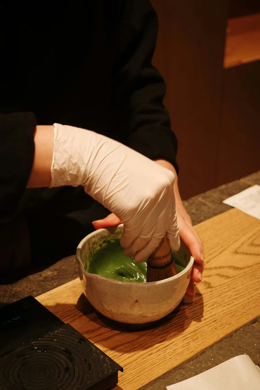 A gloved hand whisking green matcha in a ceramic bowl, illustrating tea preparation