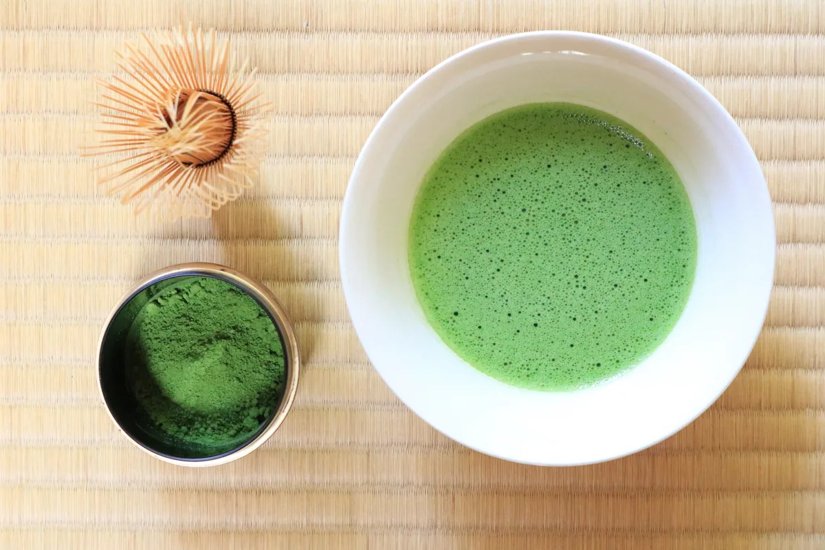 A bowl of green matcha beside tea powder and a bamboo whisk