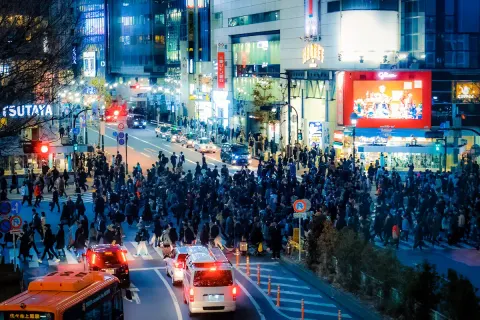 Crowds streaming across Shibuya's scramble crossing beneath neon billboards at night