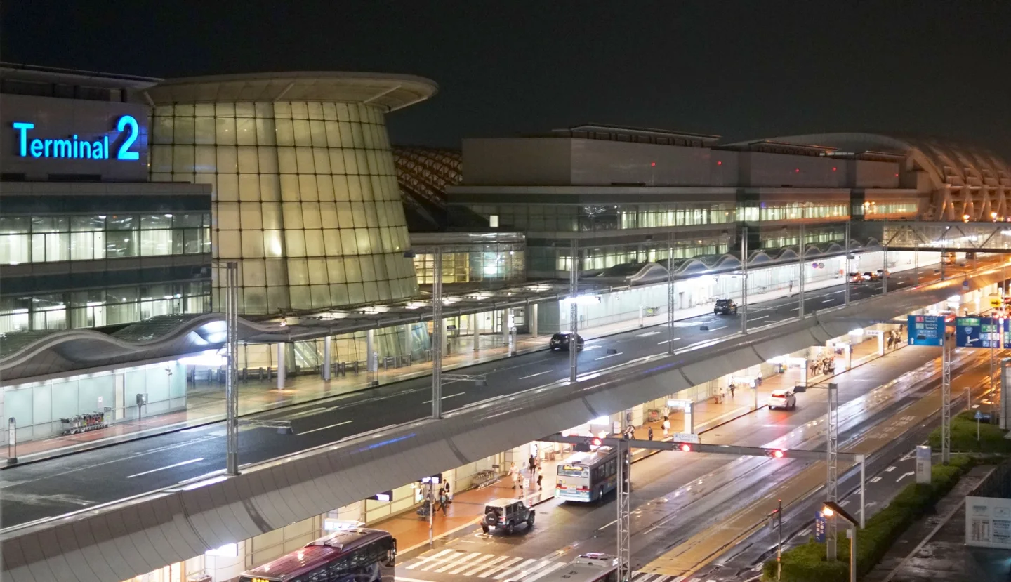 Haneda Airport Terminal 2 illuminated at night, with buses and taxis on the roads outside