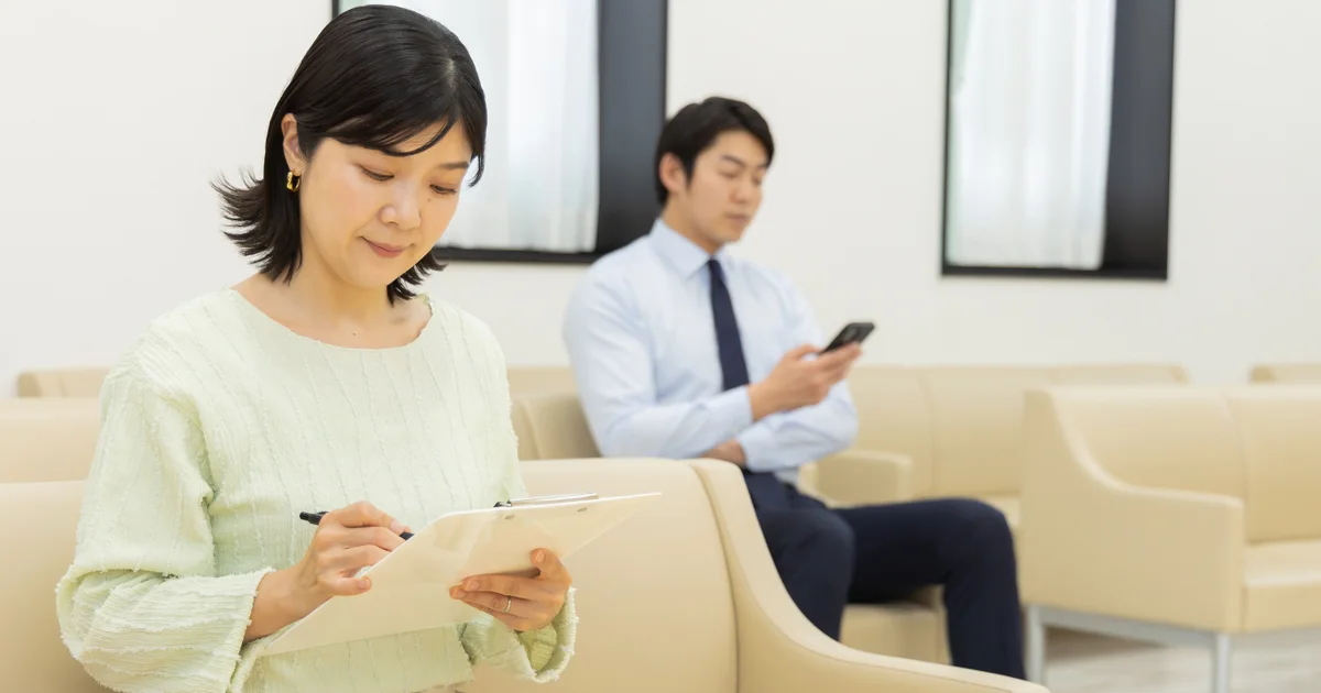 Sala de espera de una clínica japonesa: una paciente rellena el cuestionario médico mientras otro paciente espera con el móvil