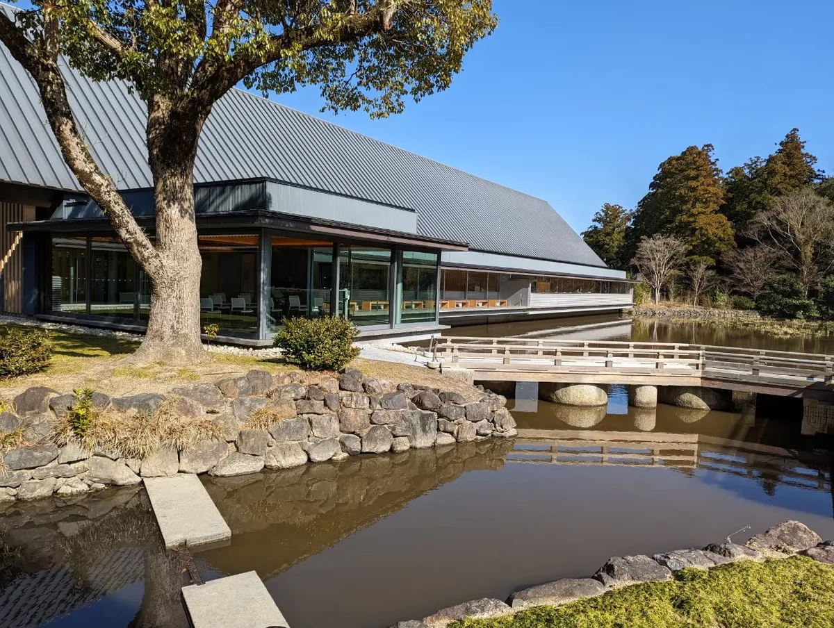 A low-roofed building and a small wooden bridge beside a pond at Ise Jingu