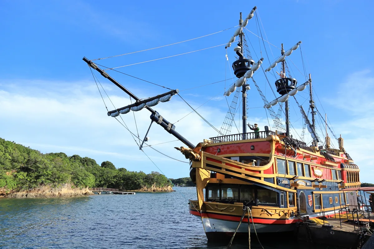 A red and gold sightseeing ship with tall masts moored on Ago Bay