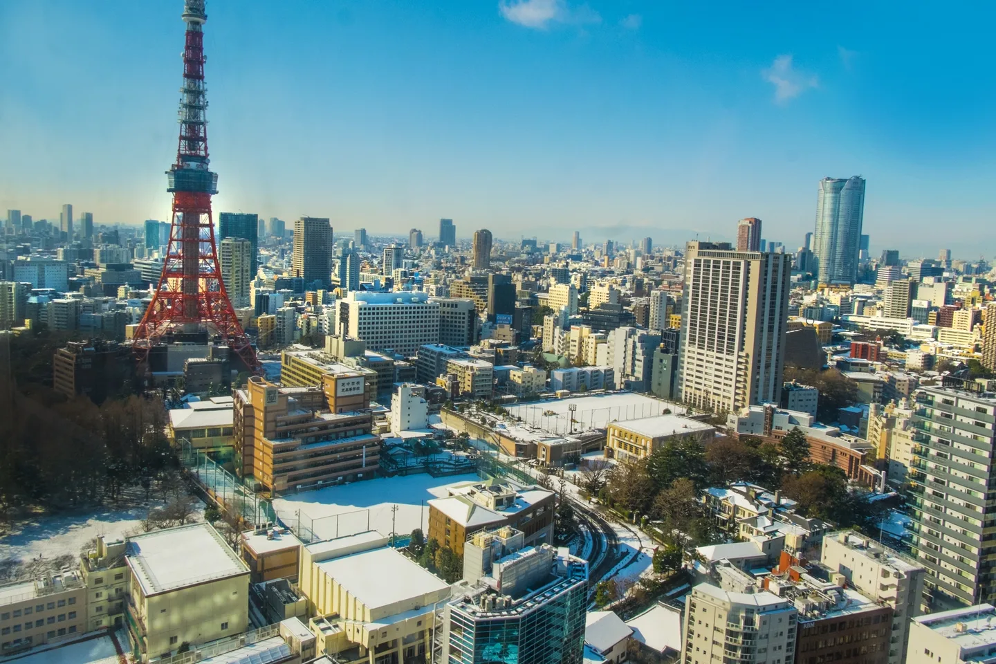 Tokyo Tower above city rooftops and a school ground covered in snow under a blue sky