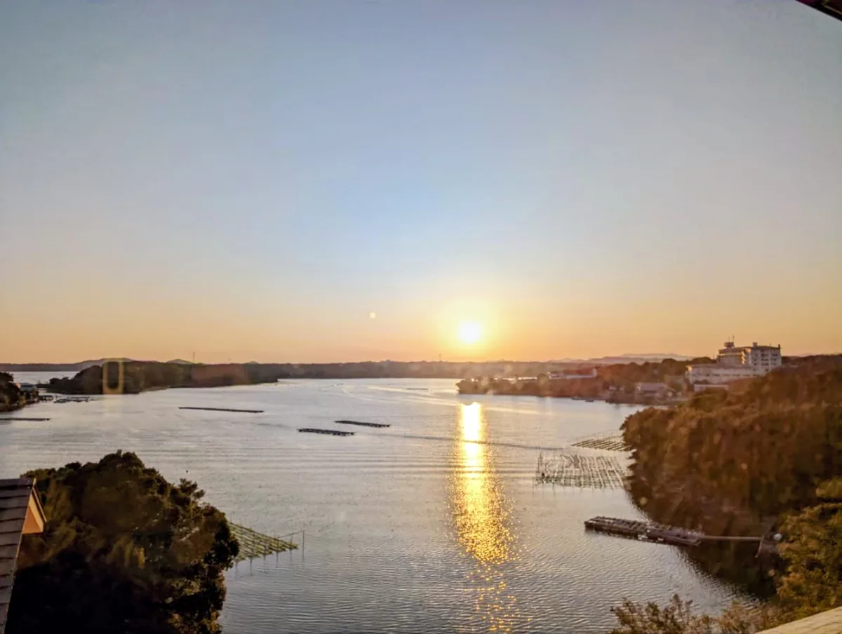 Golden sunlight reflected across Ago Bay between wooded shores and floating platforms