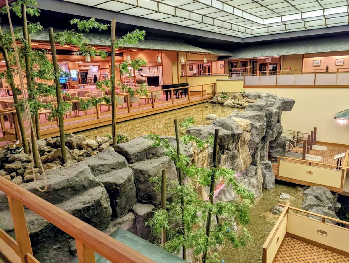 An indoor waterfall flowing over rockwork beneath walkways and greenery in Hojoen's atrium