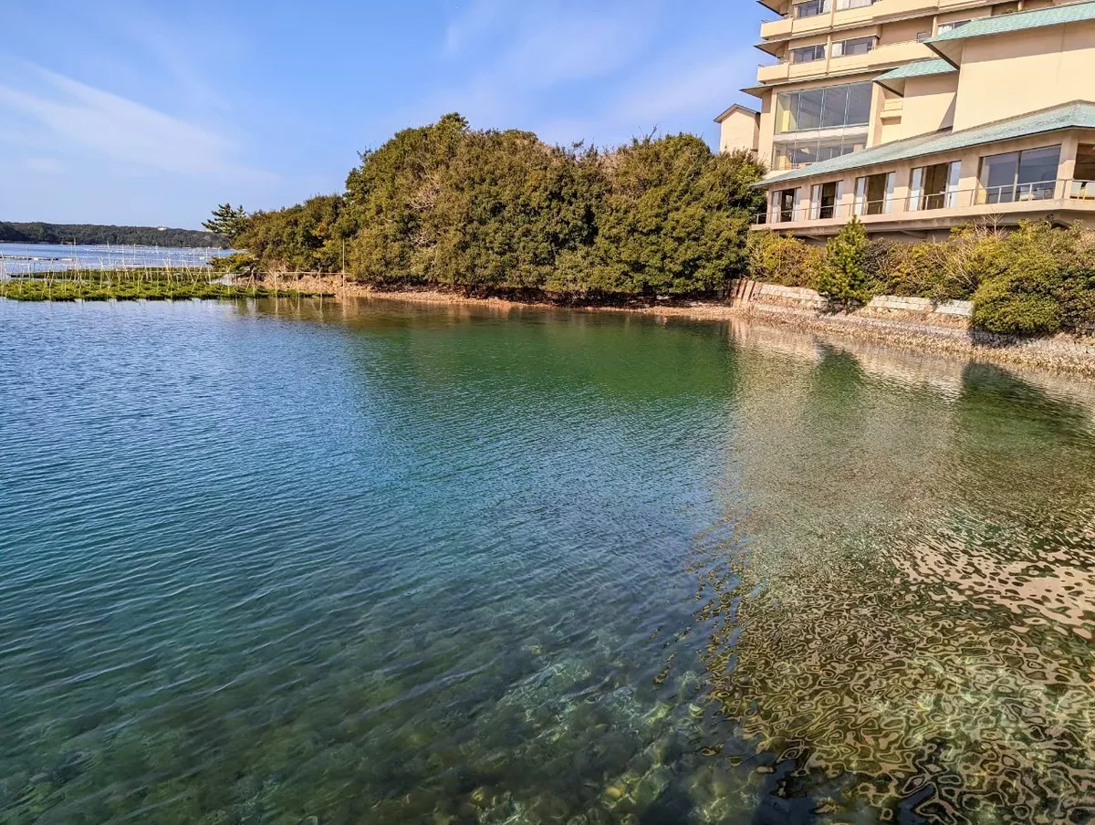 Clear water beside Hojoen's stone embankment, with trees and the hotel building along the shore