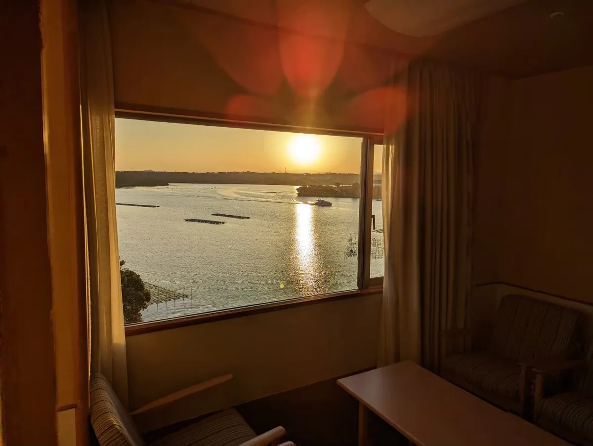 Chairs beside a guest-room window overlooking low sunlight reflected on Ago Bay
