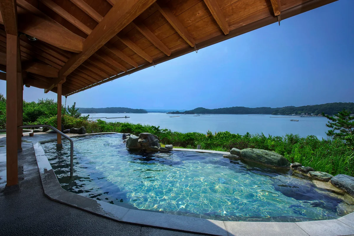 An open-air bath at Kashikojima Hojoen overlooking Ago Bay beneath a wooden roof. Illustrative image. The actual product, venue, or experience may differ.