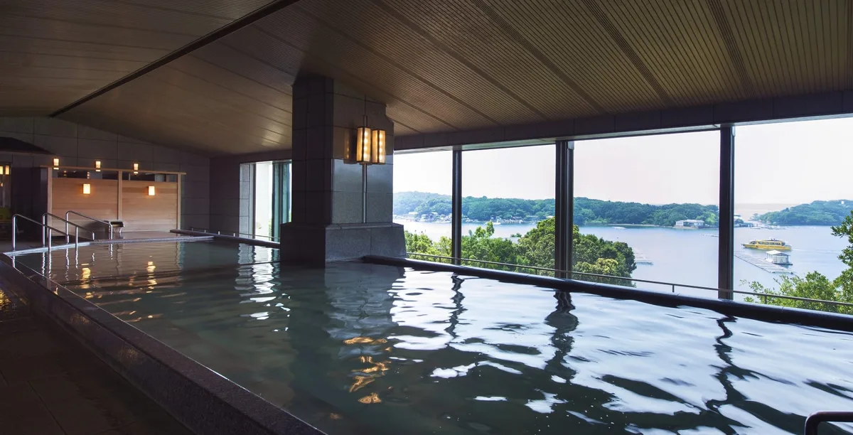 A wide indoor bathing pool beside large windows overlooking Ago Bay