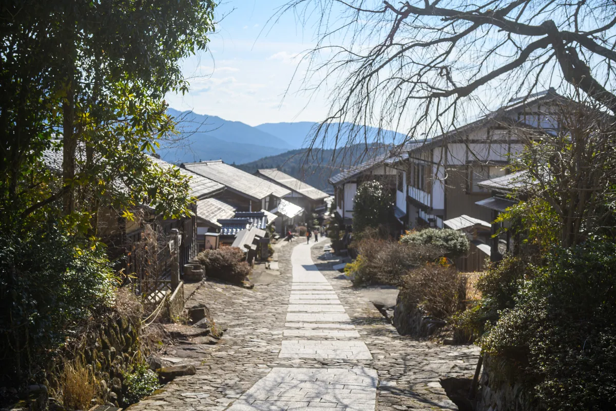 A stone-paved street descending past traditional buildings toward distant hills in Magome