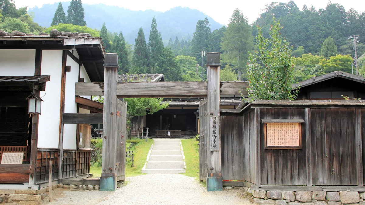 Wooden entrance gate and courtyard at Tsumago Honjin with forested hills behind