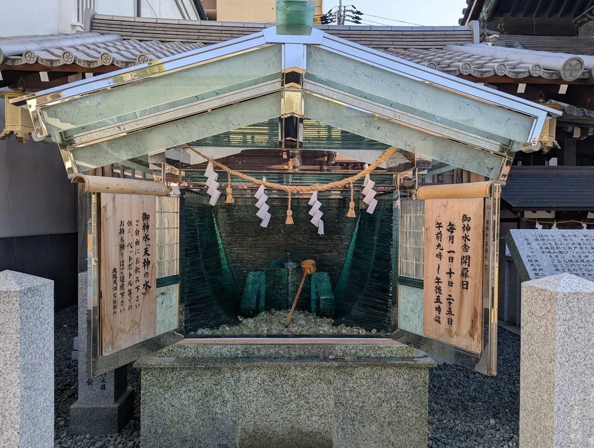 Roofed sacred-water structure with a rope and paper streamers at Osaka Tenmangu