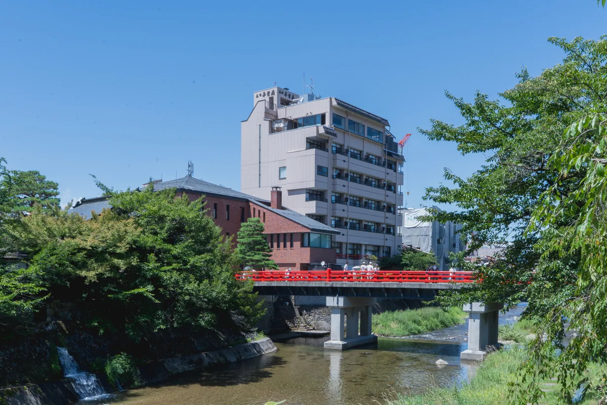 A red bridge across the Miyagawa River in Takayama with trees along the banks