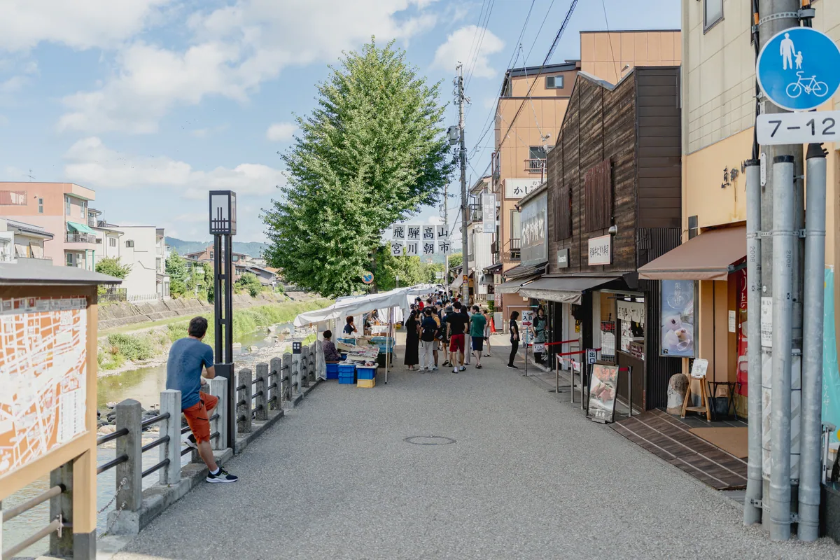 Pedestrians and shopfronts along the Miyagawa Morning Market area beside the river in Takayama