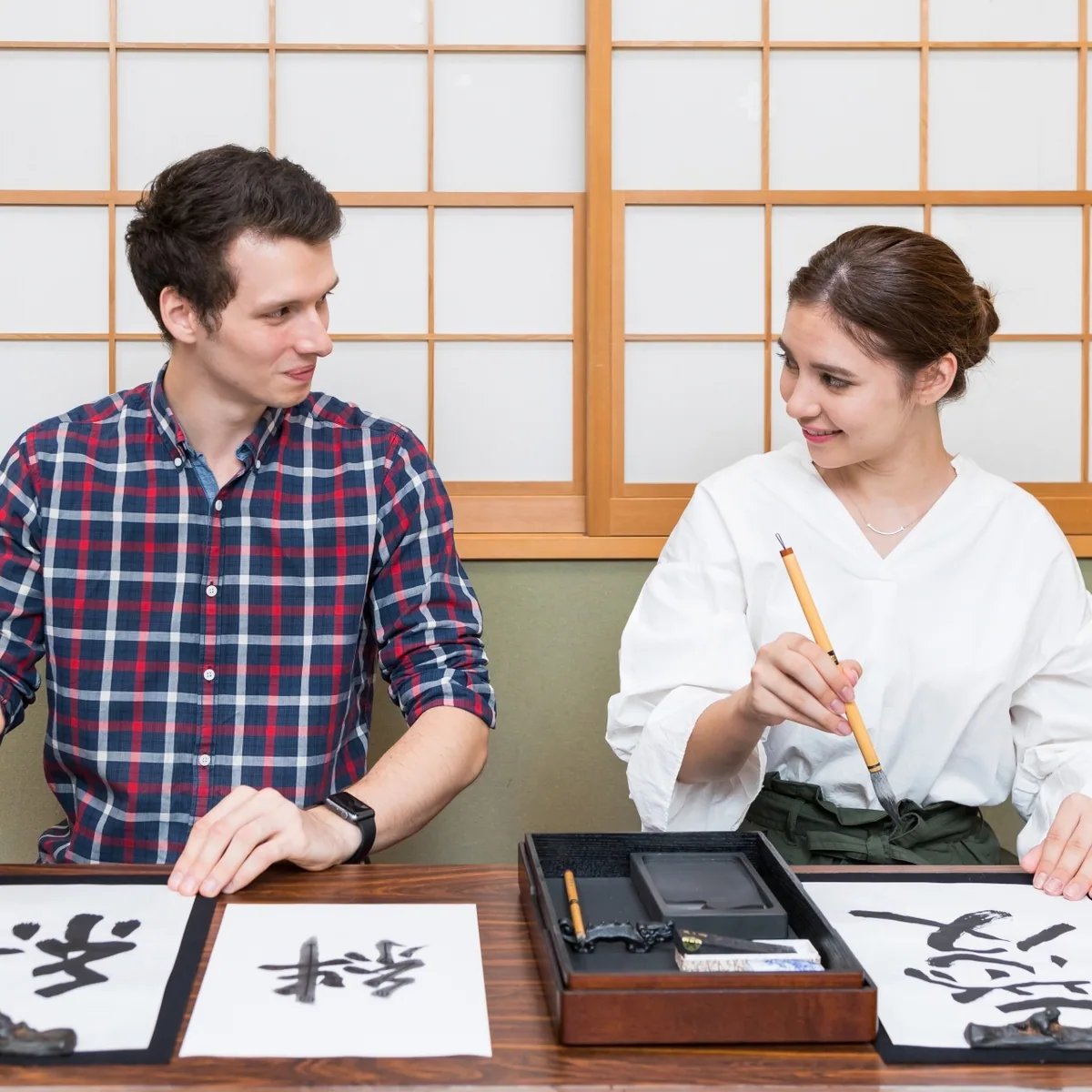 Two visitors practicing calligraphy, an illustrative photo rather than the listed workshop
