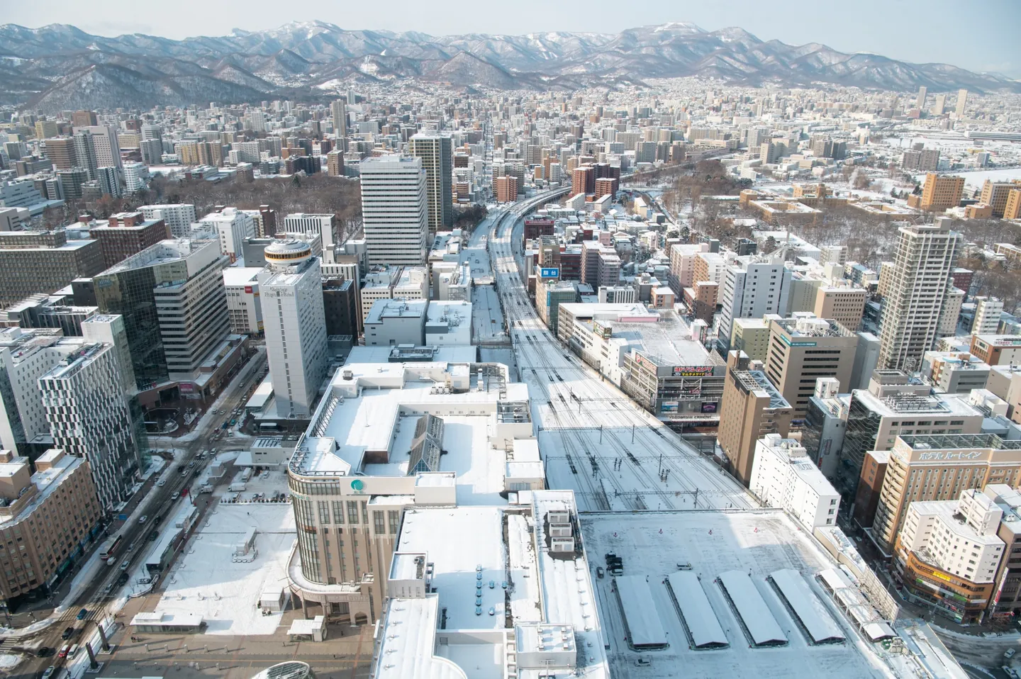 Snow-covered railway tracks and rooftops stretching across Sapporo toward the mountains
