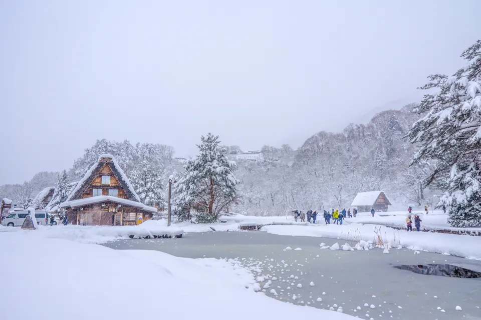Snowy gassho-style houses reflected in a pond during snowfall