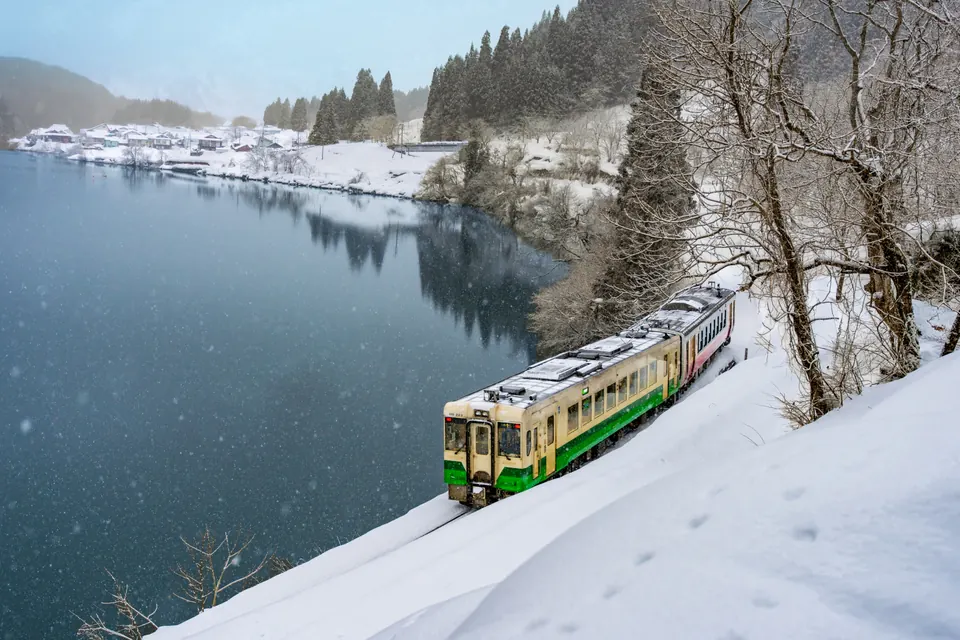 A local train following the river beside snow-covered banks and trees