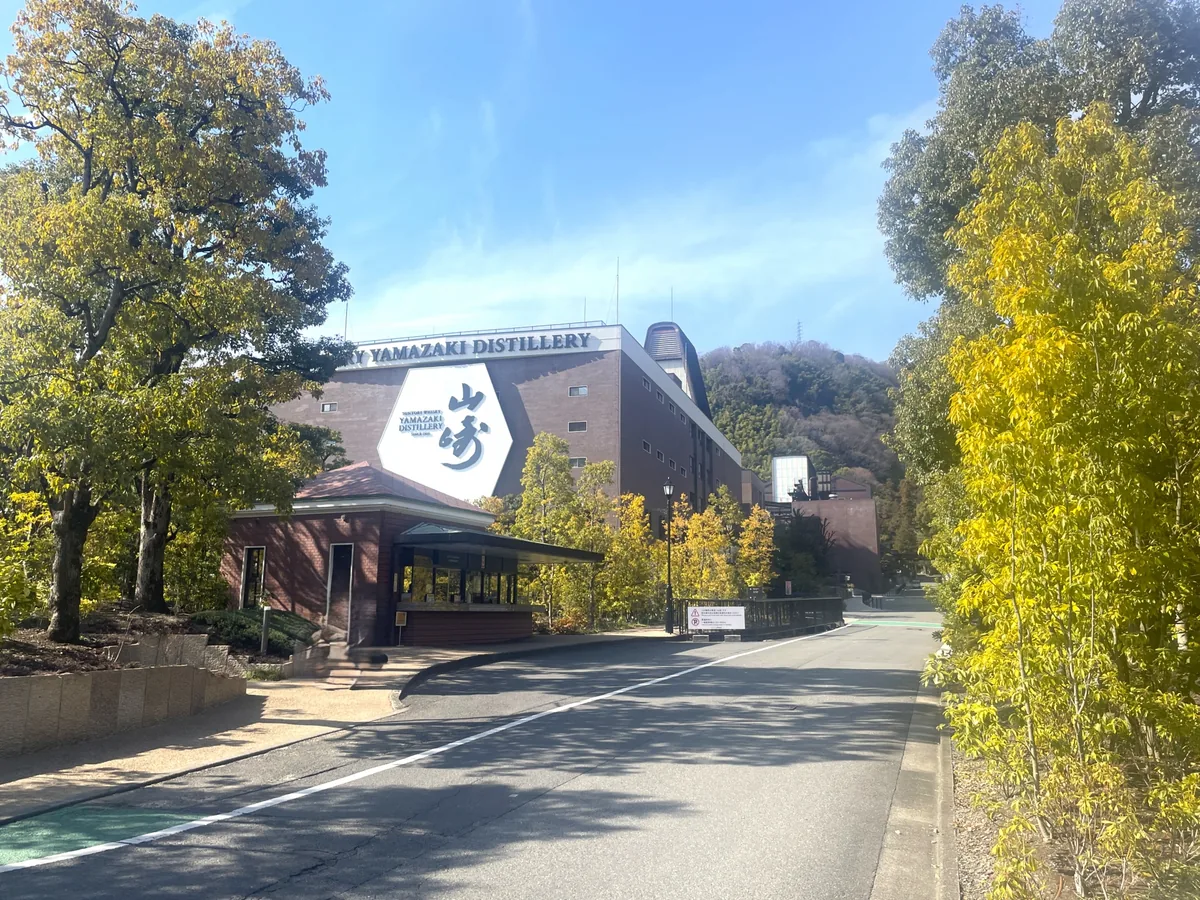 Yamazaki Distillery's brick building and large sign beside a tree-lined road