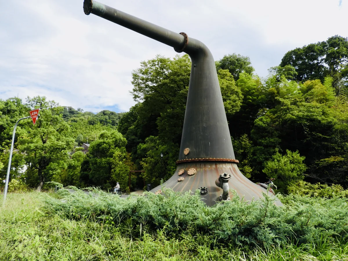 A large pot still monument surrounded by greenery in front of Yamazaki Distillery